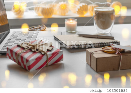 Notepad with a pen, laptop, coffee cup, wrapped gifts on a desk table. Winter Festive atmospheric mood. Preparation for Christmas. Business Holidays Concept. Freelancer's desktop during Xmas vacation Notepad with a pen, laptop, coffee cup, wrapped gifts on a desk table. Winter Festive atmospheric mood. Preparation for Christmas. Business Holidays Concept. Freelancer's desktop during Xmas vacation 108501685