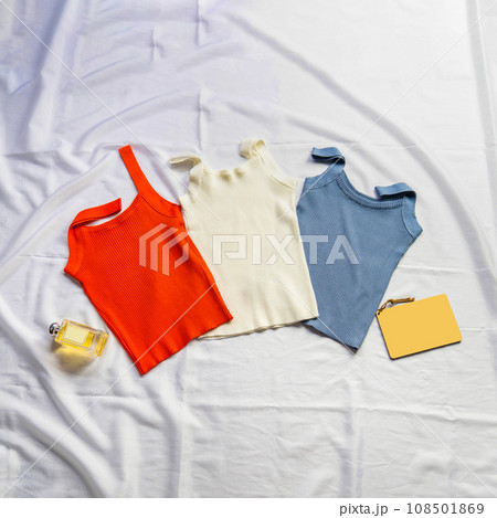 On the white sheet were three tank tops, red, white and blue, interspersed with perfume, model and notebook. On the white sheet were three tank tops, red, white and blue, interspersed with perfume, model and notebook. 108501869