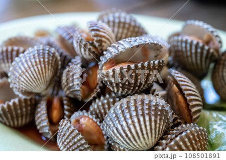 Steamed cockle or Boiled cockles on the dish with spicy seafood sauce and vegetable in restaurante wooden background Steamed cockle or Boiled cockles on the dish with spicy seafood sauce and vegetable in restaurante wooden background 108501891