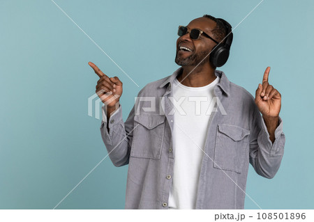 Bearded dark skinned man in headphones pointing at space for promotional content. Bearded dark skinned man in headphones pointing at space for promotional content. 108501896