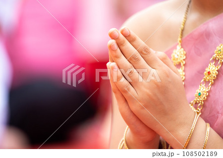 A Lady clasps her hands in front of her chest to pray. She wears .Thai traditional costume in Pink with golden traditional accessories, necklace and bracelets. . A Lady clasps her hands in front of her chest to pray. She wears .Thai traditional costume in Pink with golden traditional accessories, necklace and bracelets. . 108502189