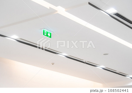 White neon sign depicting a fire exit with green background hangs from the ceiling. White neon sign depicting a fire exit with green background hangs from the ceiling. 108502441