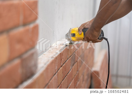 Close up worker holds Hand-Hold Sawing Machine and cuts brick foam plate board for wall installation. 108502481