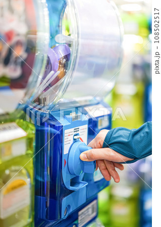 A human hand in a turquoise sweater is twisting a blue gashapon machine to release a figure. In Japan, it is considered as one of the most well liked risks. 108502517