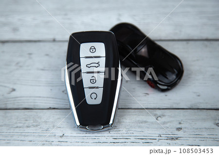 The car keys are black with metal inserts and automatic buttons lying on a background of white wood, next to it is a black car with a close-up plan. High quality photo 108503453