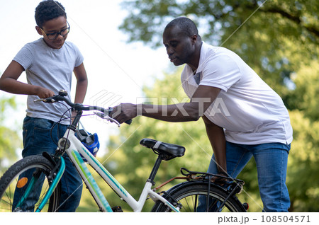 Dark-skinned man fixing a bike in the park Dark-skinned man fixing a bike in the park 108504571
