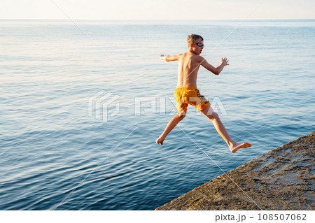Healthy boy jumps into tranquil ocean water from stone pier Healthy boy jumps into tranquil ocean water from stone pier 108507062