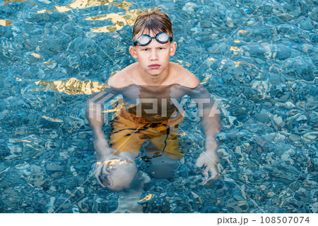 Grumpy boy swims with goggles swims in clear ocean water 108507074