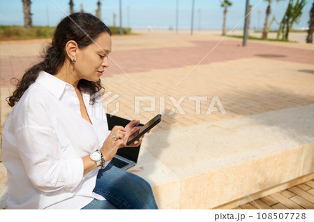 Young woman using smartphone checks social media content outdoors, messaging, browsing new app, online shopping, booking 108507728