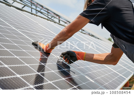Close up of man hands in work gloves mounting photovoltaic solar panels. Male worker assembling solar modules for generating electricity through photovoltaic effect. Renewable energy sources concept. 108508454