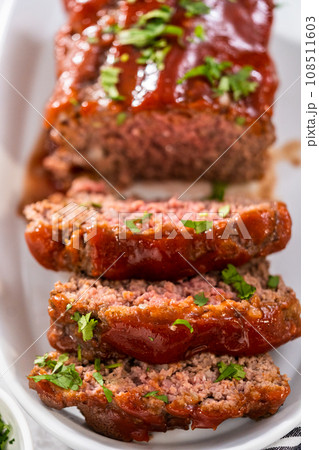 Slicing classic meatloaf with a sweet glaze on a white serving plate Slicing classic meatloaf with a sweet glaze on a white serving plate 108511603