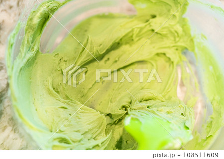 In a well-lit kitchen, an assortment of buttercream frosting in various shades of green and other colors is being meticulously mixed and prepared for the artistic decoration of cupcakes in charming In a well-lit kitchen, an assortment of buttercream frosting in various shades of green and other colors is being meticulously mixed and prepared for the artistic decoration of cupcakes in charming 108511609