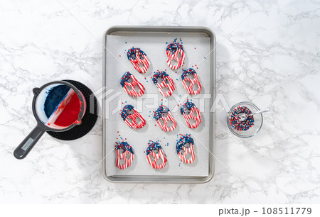 Flat lay. Dipping pretzels twists into melted chocolate to make red, white, and blue chocolate-covered pretzel twists. Flat lay. Dipping pretzels twists into melted chocolate to make red, white, and blue chocolate-covered pretzel twists. 108511779