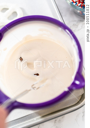 Dipping pretzels twists into melted chocolate to make red, white, and blue chocolate-covered pretzel twists. 108511812