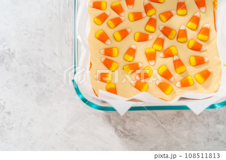 Removing candy corn fudge from a square glass baking pan lined with parchment. 108511813