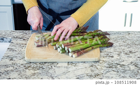 Large organic asparagus stalks are being sliced in a modern white kitchen, in preparation for steaming. Large organic asparagus stalks are being sliced in a modern white kitchen, in preparation for steaming. 108511908