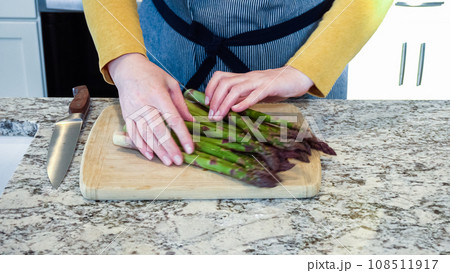 Large organic asparagus stalks are being sliced in a modern white kitchen, in preparation for steaming. 108511917