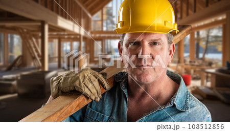 Male Contractor at a Construction Site Wearing a Hard Hat and Work Gloves Holding Lumber 2x4. . Male Contractor at a Construction Site Wearing a Hard Hat and Work Gloves Holding Lumber 2x4. . 108512856
