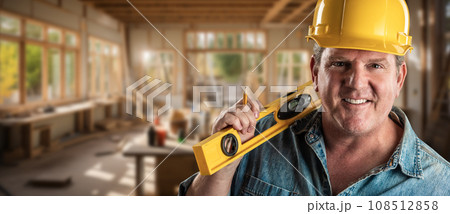 Hard Working Male Contractor at a Construction Site Wearing a Hard Hat and Work Gloves Holding His Level. Hard Working Male Contractor at a Construction Site Wearing a Hard Hat and Work Gloves Holding His Level. 108512858