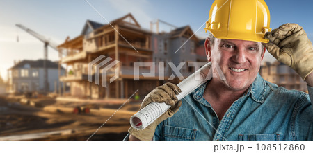Friendly Male Contractor at a Construction Site Wearing a Hard Hat and Work Gloves Holding His Blueprint Plans. Friendly Male Contractor at a Construction Site Wearing a Hard Hat and Work Gloves Holding His Blueprint Plans. 108512860