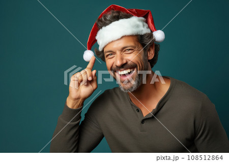 Funny man, happy guy pointing finger to strange Santa hat. Portrait of smiling person isolated on blue green studio background. Concept of Christmas, show, welcome, xmas, fun, people Funny man, happy guy pointing finger to strange Santa hat. Portrait of smiling person isolated on blue green studio background. Concept of Christmas, show, welcome, xmas, fun, people 108512864