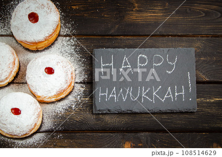 Happy Hanukkah. Traditional dessert Sufganiyot on dark wooden background. Donuts, candles and gifts. Celebrating Jewish holiday. 108514629