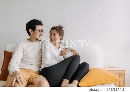 Happy lovely asian couple sharing smartphone to watch together in living room 108515154