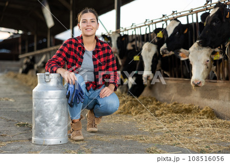 Smiling girl dairy farm worker posing with milk can in cowshed 108516056
