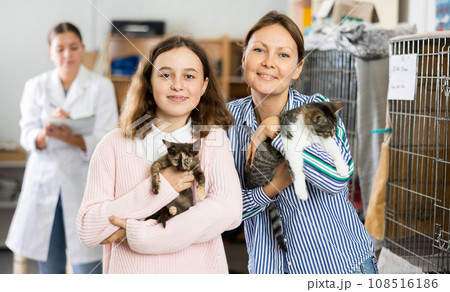 Preteen girl with mother standing in animal shelter holding cats Preteen girl with mother standing in animal shelter holding cats 108516186