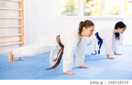 Two women in kimonos doing stretching before karate ore judo training 108516554