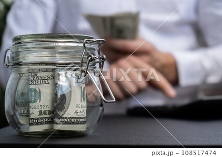 Dollar Banknote Saving Money In Glass Jar. Unrecognizable man calculate money on calculator Moderate Consumption And Economy Collecting Money Tips Business Finance 108517474