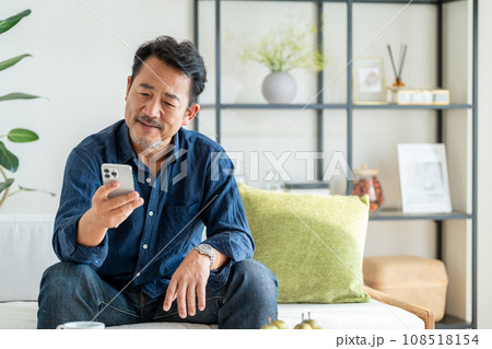 リビングでスマートフォンを使うシニア男性。 108518154