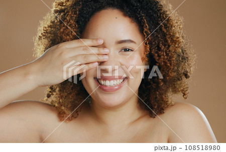 Portrait, funny or happy woman with natural beauty dermatology for wellness in studio with smile. Hand, eye cover or biracial female person laughing with skincare, pride or glow on brown background 108518980