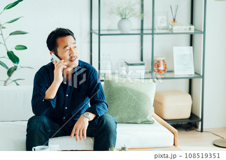 リビングでスマートフォンを使うシニア男性。 108519351