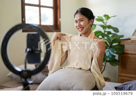 A beautiful female influencer or online seller is showing and reviewing her clothes to the camera. A beautiful female influencer or online seller is showing and reviewing her clothes to the camera. 108519679