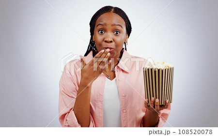 Portrait, surprise or black woman watching movie in studio for cinema with popcorn to relax. Omg, wow or shocked African person eating snack for streaming film or subscription on grey background Portrait, surprise or black woman watching movie in studio for cinema with popcorn to relax. Omg, wow or shocked African person eating snack for streaming film or subscription on grey background 108520078