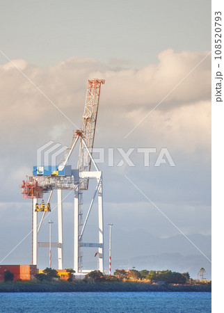 A crane and shipping containers in a shipyard surrounded by the ocean. Industrial hoisting crane in a logistics or cargo harbor at a seaport for the transportation of liquid materials A crane and shipping containers in a shipyard surrounded by the ocean. Industrial hoisting crane in a logistics or cargo harbor at a seaport for the transportation of liquid materials 108520793