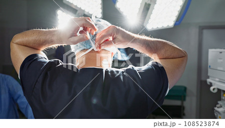 Surgery, preparation and doctor tie mask in operating room for medical service, protection and operation. Healthcare ppe, safety scrubs and person with uniform for emergency, procedure and wellness 108523874