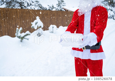 Food delivery service containers in hands of Santa Claus outdoor in snow. Christmas eve promotion. Ready-made hot order, disposable plastic box. New year holidays catering. Copy space, mock up Food delivery service containers in hands of Santa Claus outdoor in snow. Christmas eve promotion. Ready-made hot order, disposable plastic box. New year holidays catering. Copy space, mock up 108526078
