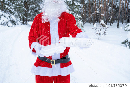 Food delivery service containers in hands of Santa Claus outdoor in snow. Christmas eve promotion. Ready-made hot order, disposable plastic box. New year holidays catering. Copy space, mock up 108526079