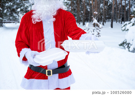 Food delivery service containers in hands of Santa Claus outdoor in snow. Christmas eve promotion. Ready-made hot order, disposable plastic box. New year holidays catering. Copy space, mock up Food delivery service containers in hands of Santa Claus outdoor in snow. Christmas eve promotion. Ready-made hot order, disposable plastic box. New year holidays catering. Copy space, mock up 108526080