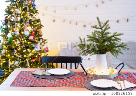 Serving a festive table with plates, forks, knives, napkins, glasses close-up in the modern interior of a loft house decorated for Christmas and New Year. Waiting for guests for a festive dinner Serving a festive table with plates, forks, knives, napkins, glasses close-up in the modern interior of a loft house decorated for Christmas and New Year. Waiting for guests for a festive dinner 108526155