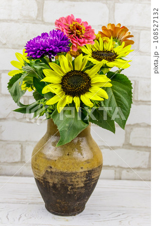 Bouquet of flowers in antique rustic clay jug against white brick wall 108527132