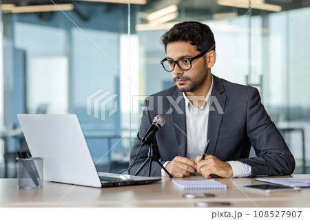 Concentrated serious and confident businessman financier inside office at workplace using professional microphone to record online video course and podcast, business trainer coach in business suit. Concentrated serious and confident businessman financier inside office at workplace using professional microphone to record online video course and podcast, business trainer coach in business suit. 108527907