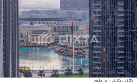 Aerial view of Dubai Fountain in downtown with palms in park next to shopping mall and souq night to day timelapse, UAE 108531109