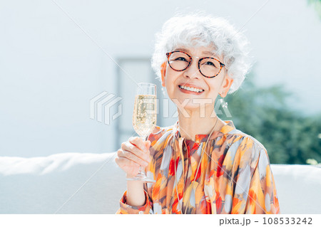 自宅の庭でシャンパンを飲むシニアの女性 自宅の庭でシャンパンを飲むシニアの女性 108533242