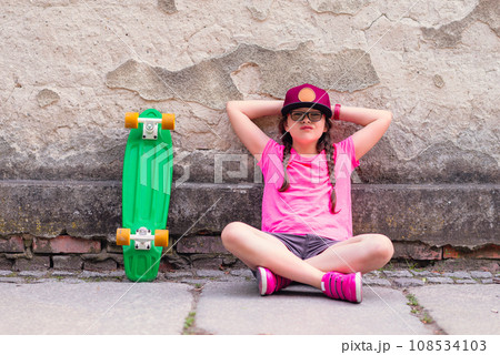 Portrait of a little girl sitting on the ground with a skateboard Portrait of a little girl sitting on the ground with a skateboard 108534103