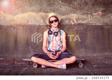 Portrait of a teenage girl sitting on a skateboard  108534175