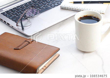 机にノートパソコンやノートを広げ、コーヒーを飲みながらデスクワークをしているイメージ 108534675