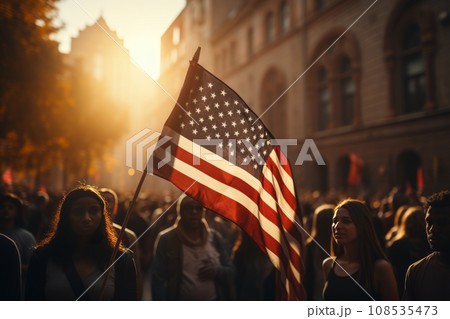 A huge crowd of people marches along a city street with American flags. The Stars and Stripes flutter over people's heads. Independence Day 4th of July concept. The US main holiday. National pride. A huge crowd of people marches along a city street with American flags. The Stars and Stripes flutter over people's heads. Independence Day 4th of July concept. The US main holiday. National pride. 108535473